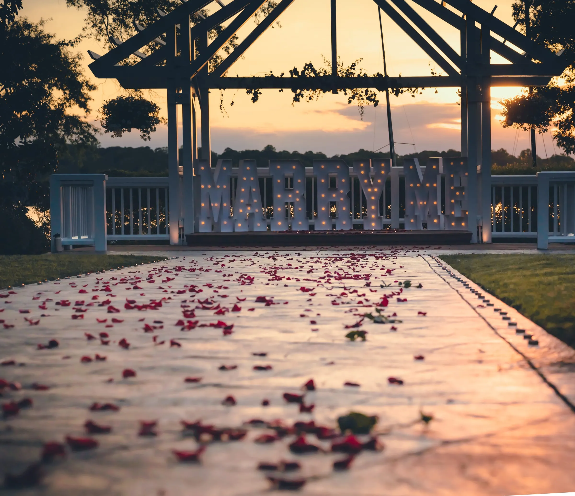 A path scattered with red rose petals leading to the lakeside pavilion at golden hour