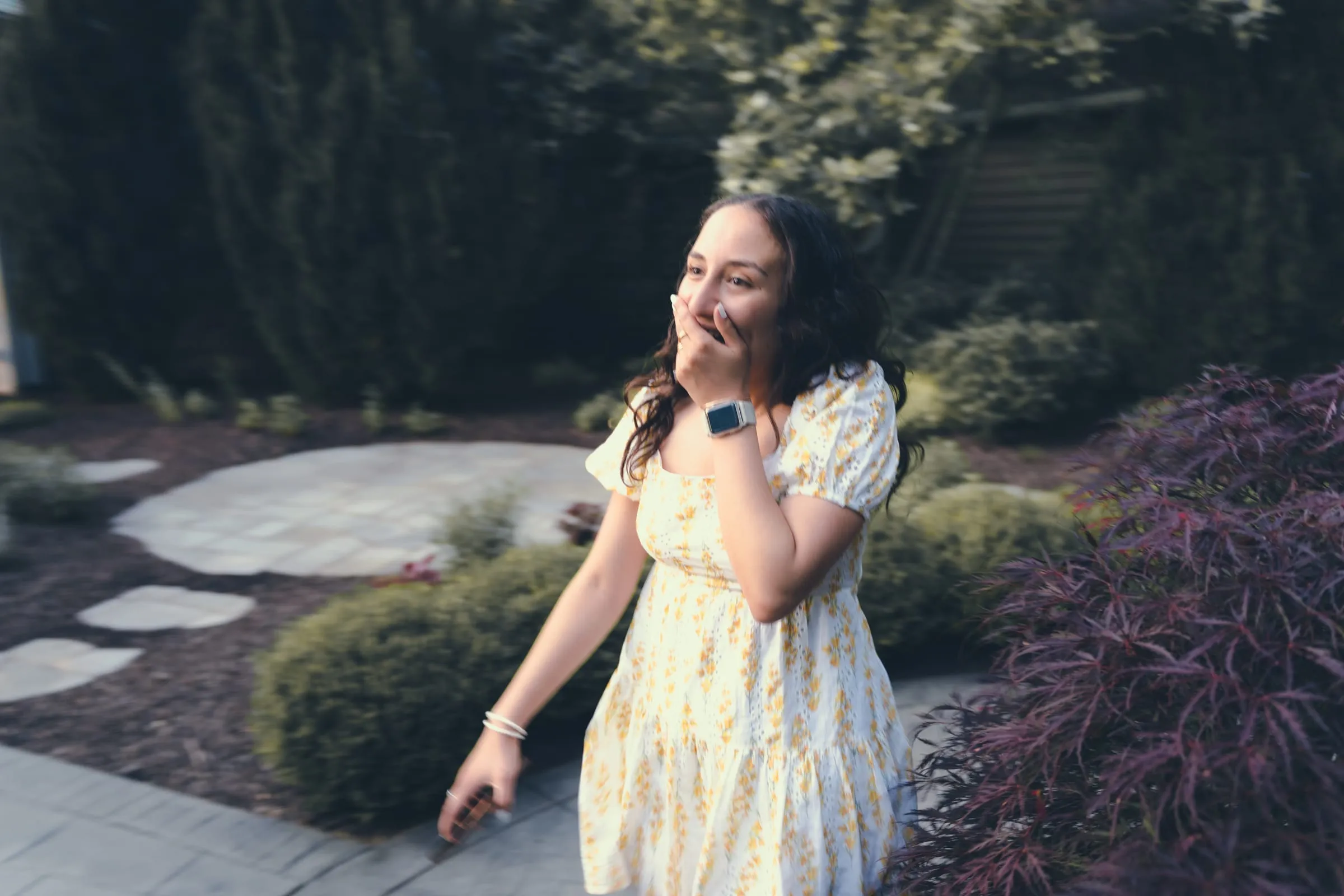 Marina covering a smile with one hand while walking up the garden path