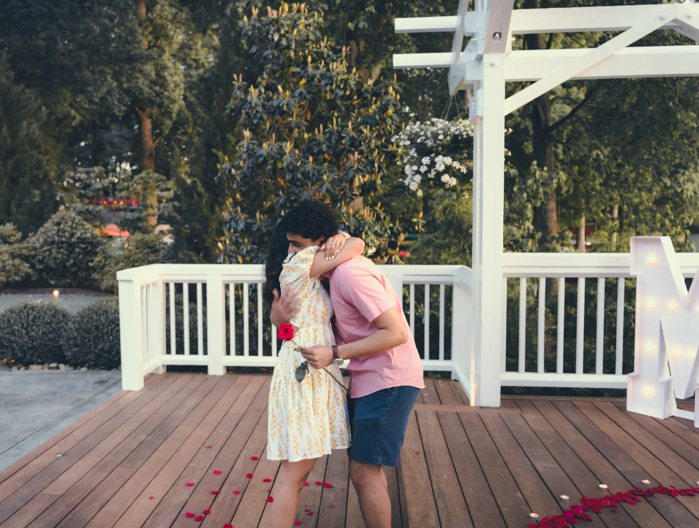 Marina and George hugging on the pavilion deck, a red rose in hand