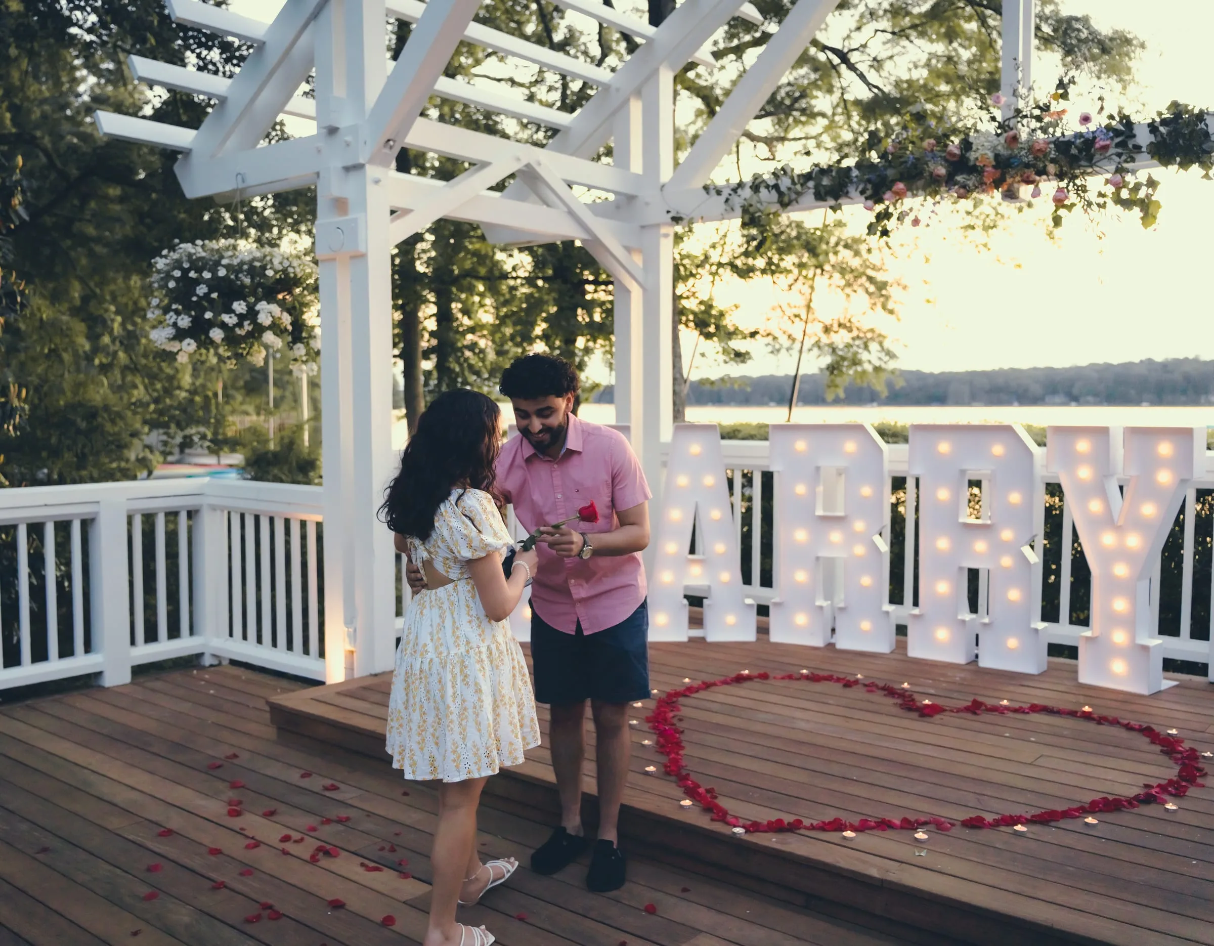George opening the ring box for Marina beside the MARRY ME letters and rose petal heart