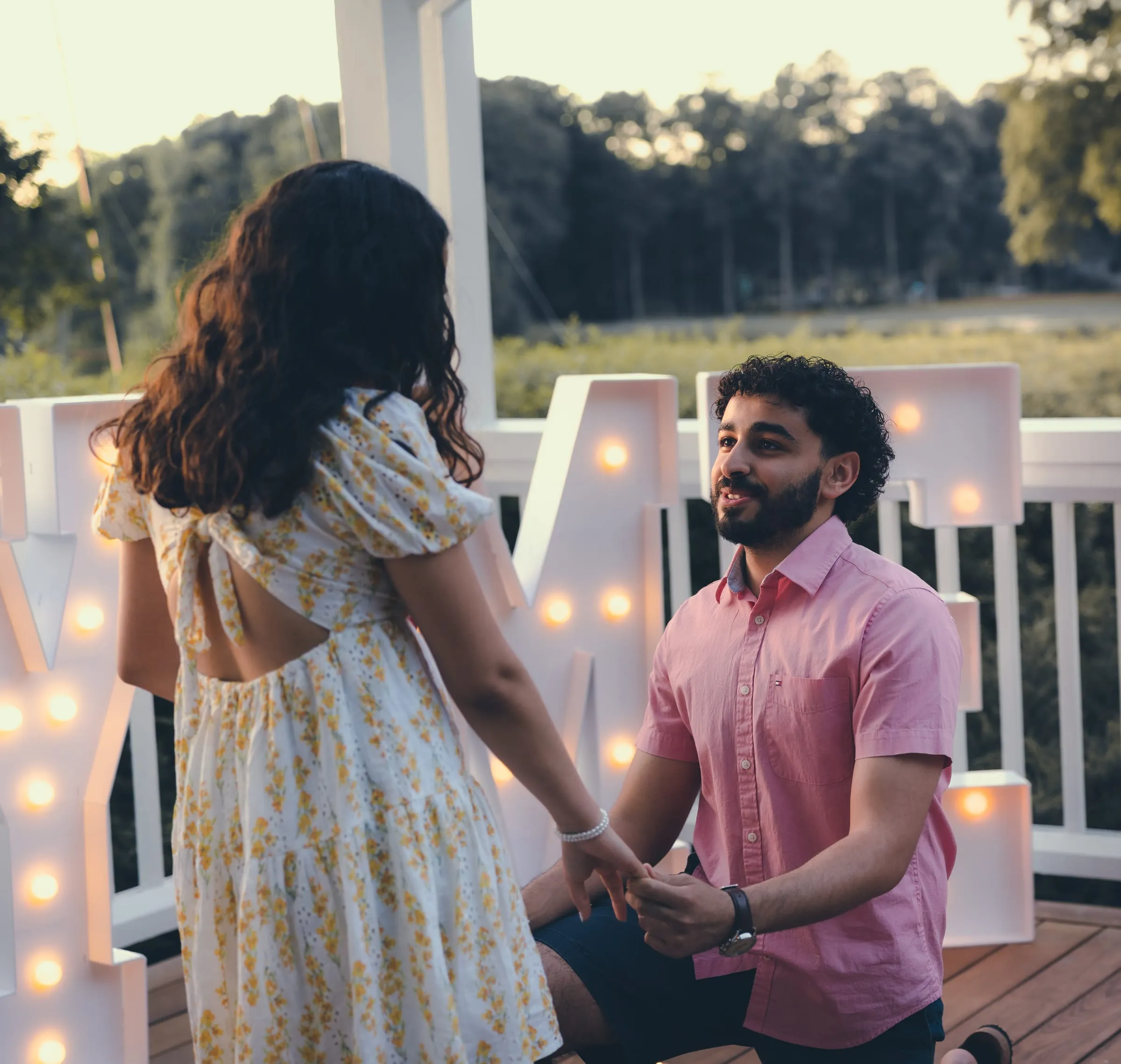 George smiling up at Marina from one knee between the lit letters