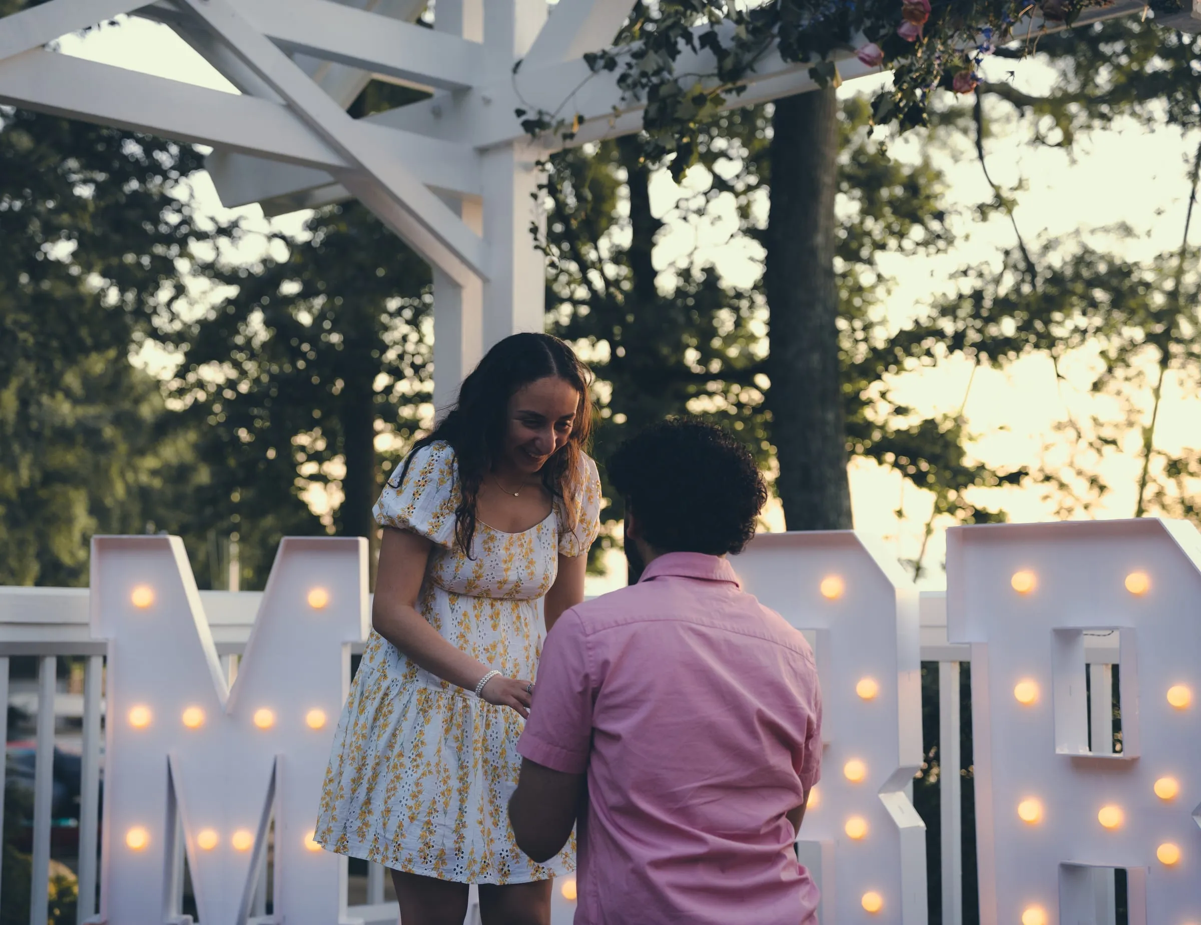 Marina laughing while George places the ring, the lit letters on either side