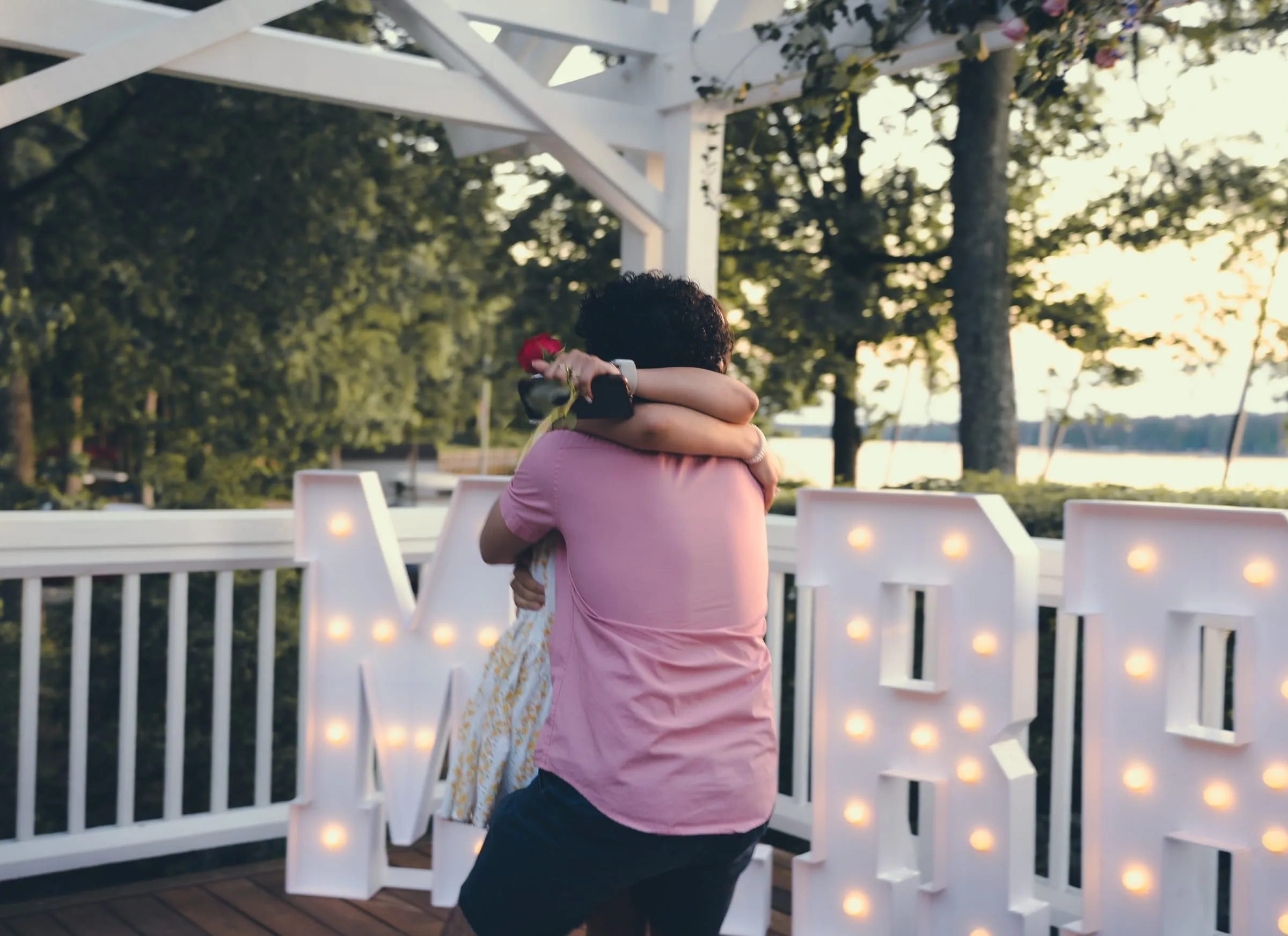 Marina and George in a tight embrace after the yes, a rose in hand