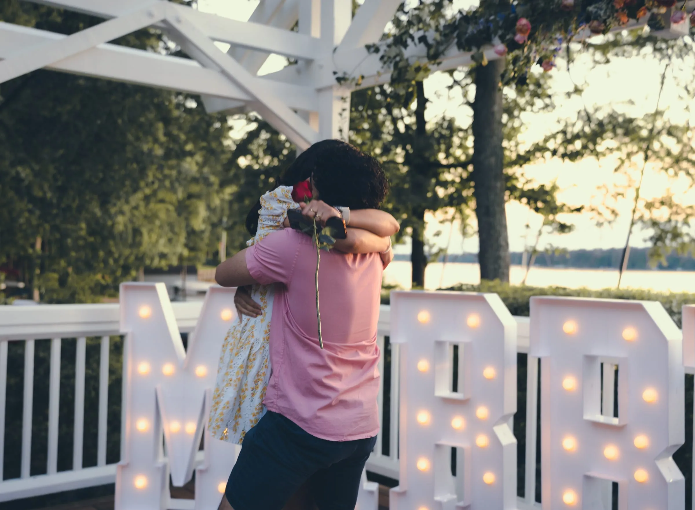 Marina and George holding each other close in front of the MARRY ME letters