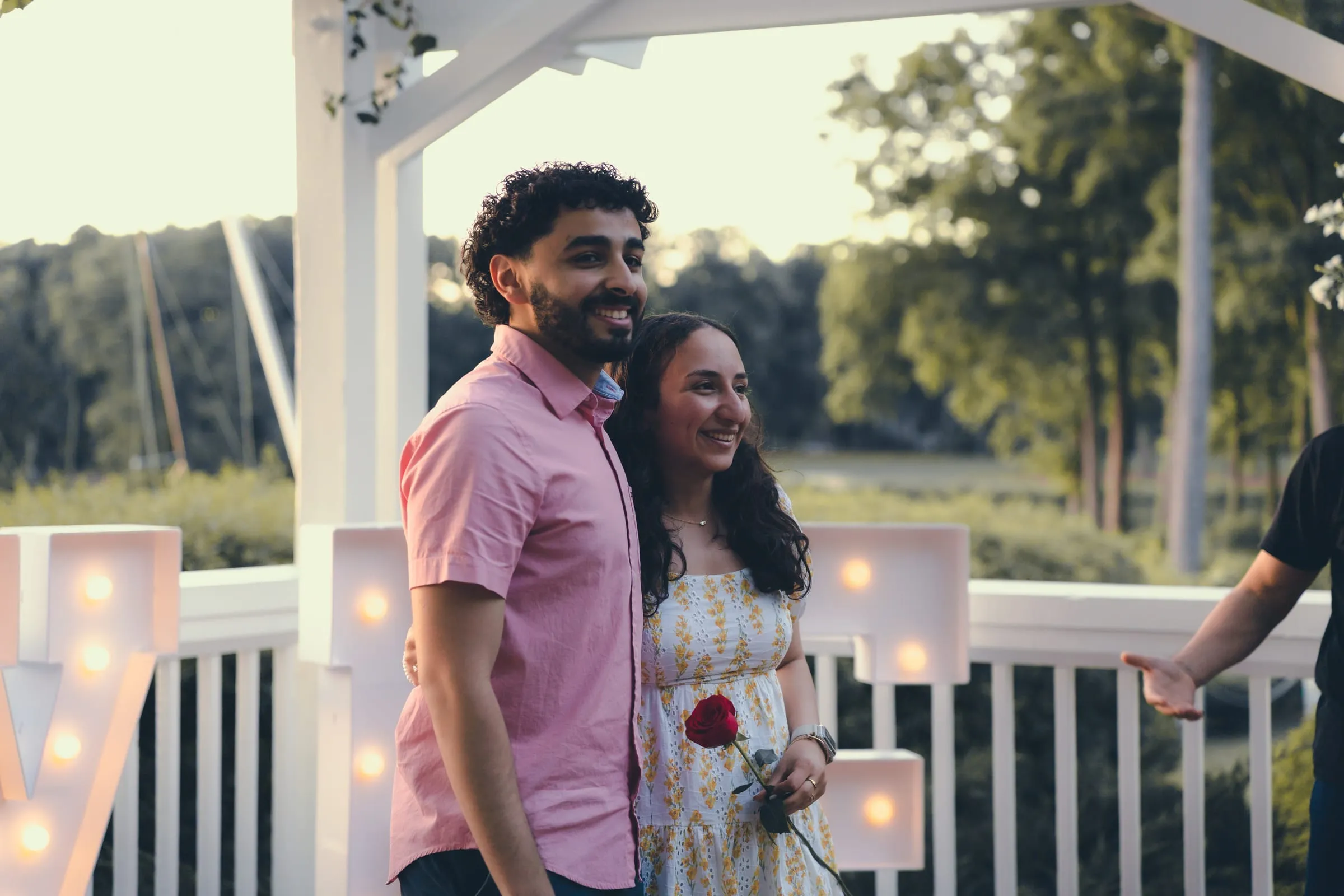 Marina and George smiling together with a single red rose, the lake behind them