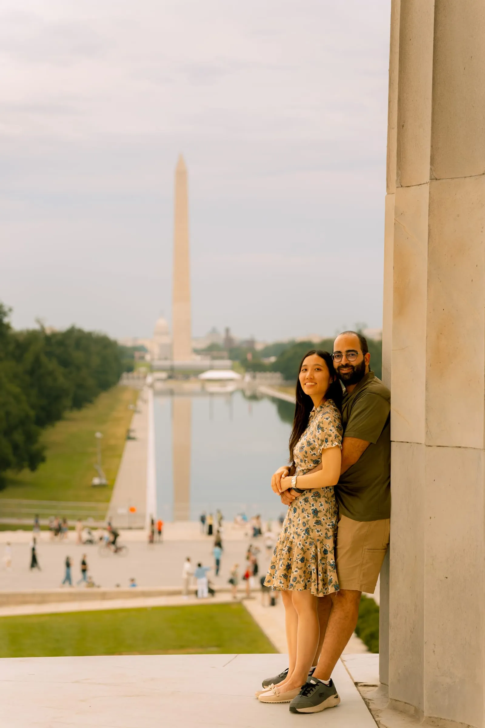 Maryann and Samuel embracing beside a column with the Washington Monument in the distance