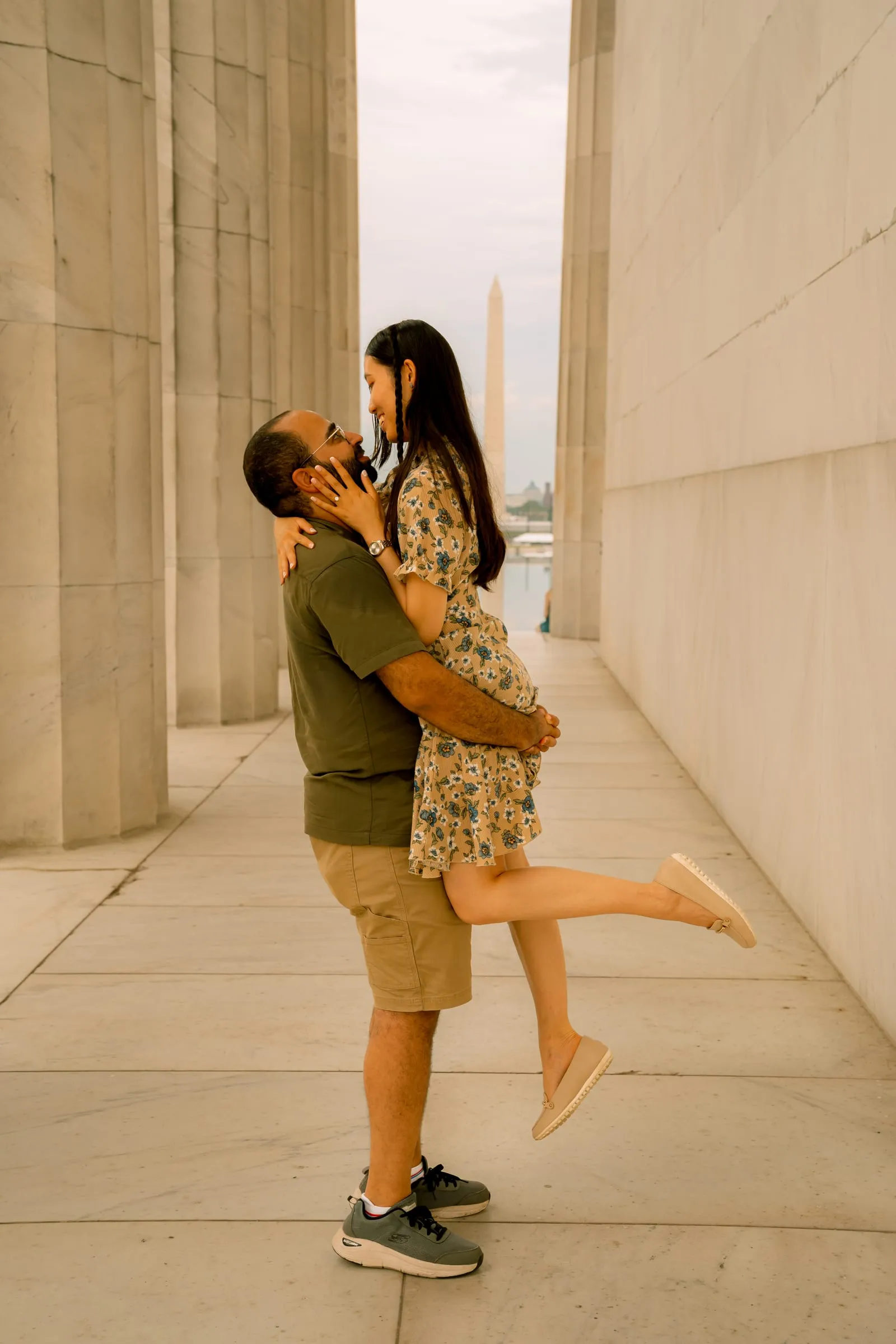 Maryann kicking up her leg as Samuel lifts her between the columns, the Washington Monument beyond