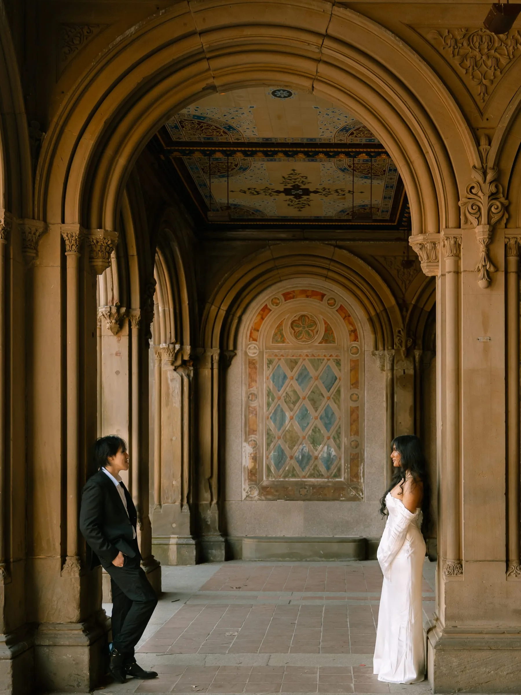 Noushin and Nathan leaning against opposite columns of the arcade, looking at each other