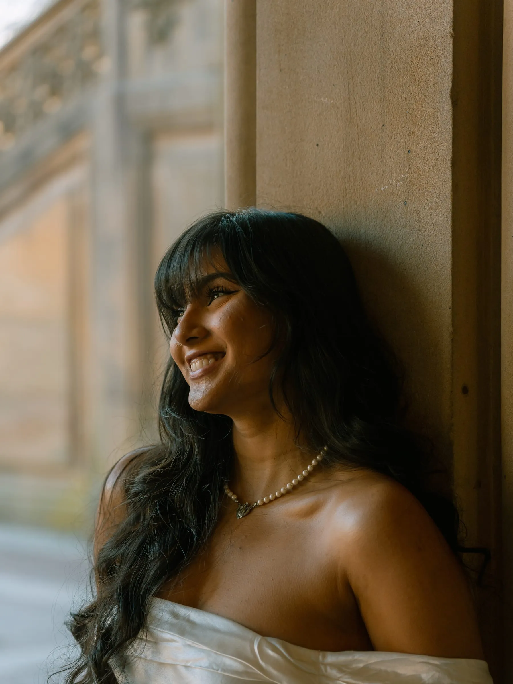 Noushin smiling and looking off to the side, leaning against a sandstone column