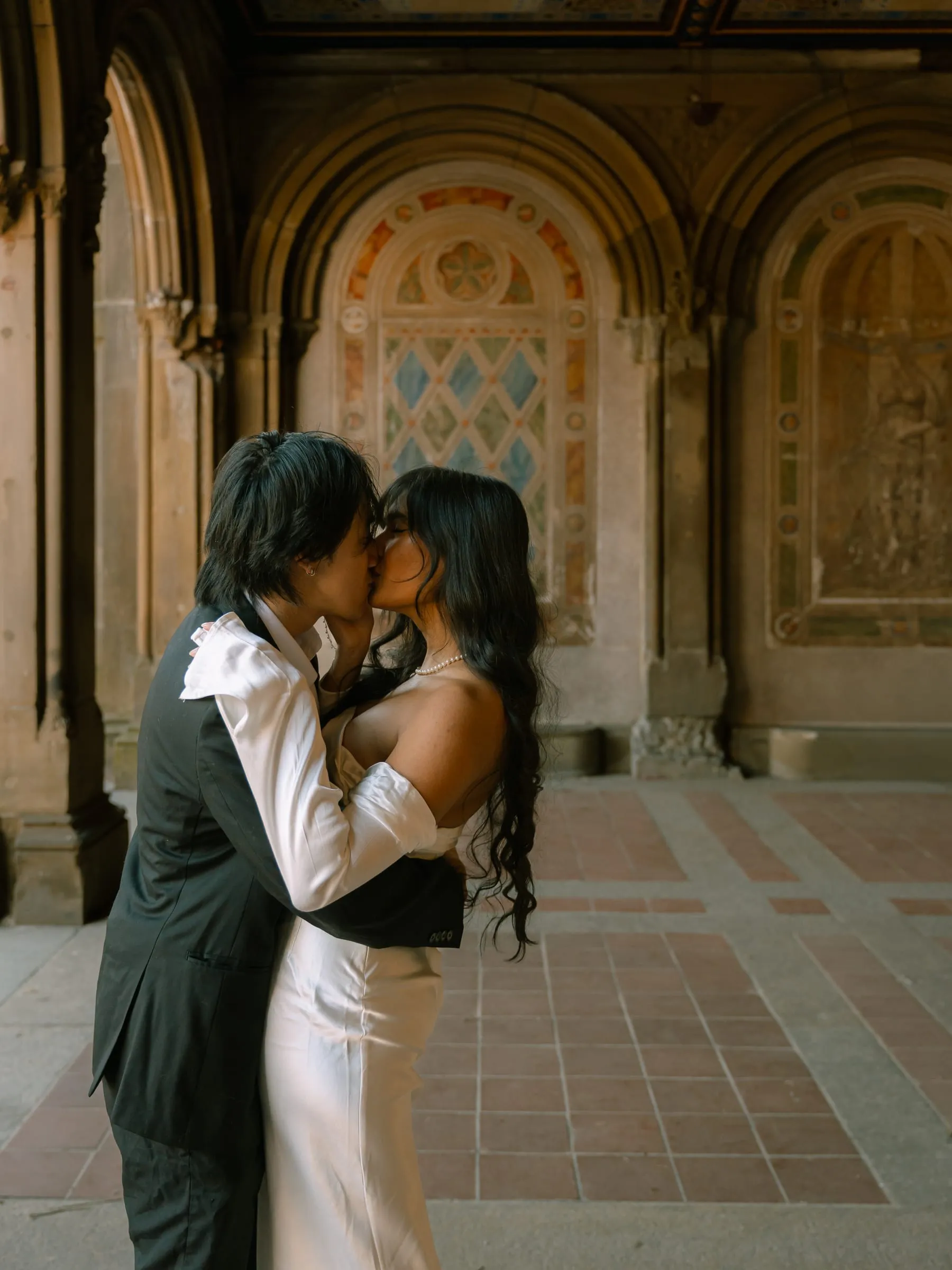 Noushin and Nathan sharing a kiss beneath the painted stone arches