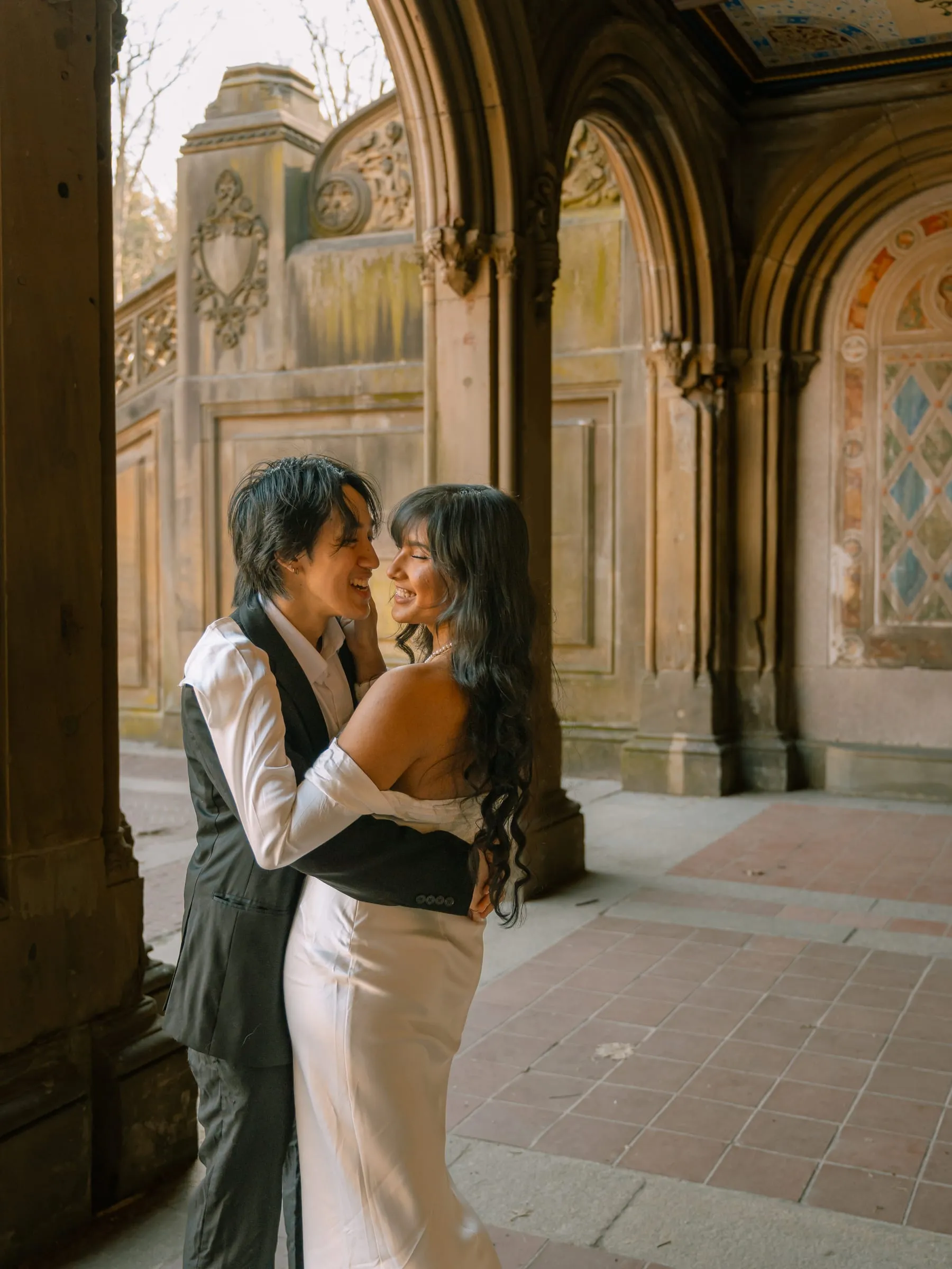 Noushin and Nathan laughing in each other's arms beside a column of the arcade
