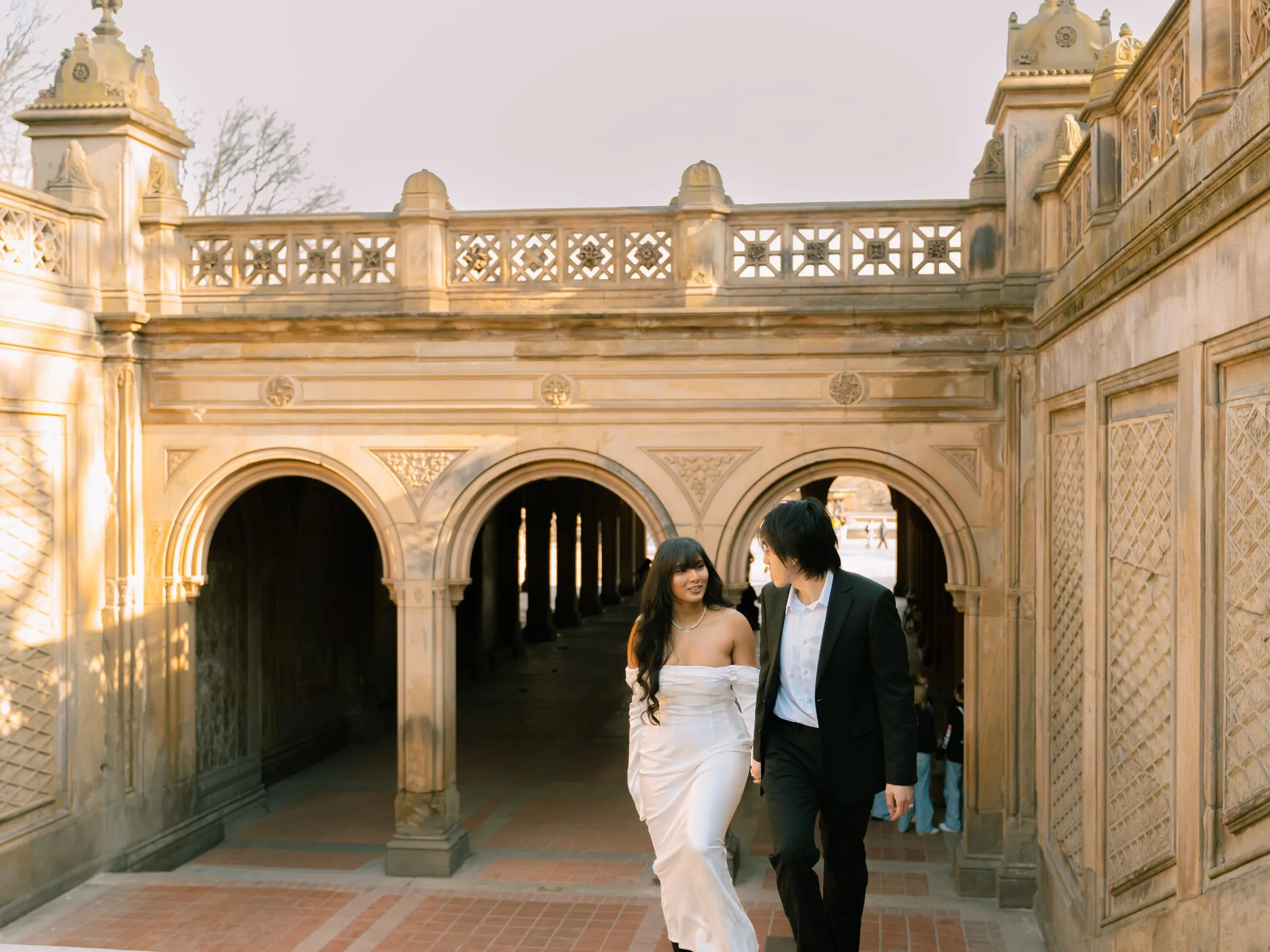 Noushin and Nathan walking together through Bethesda Terrace's stone underpass