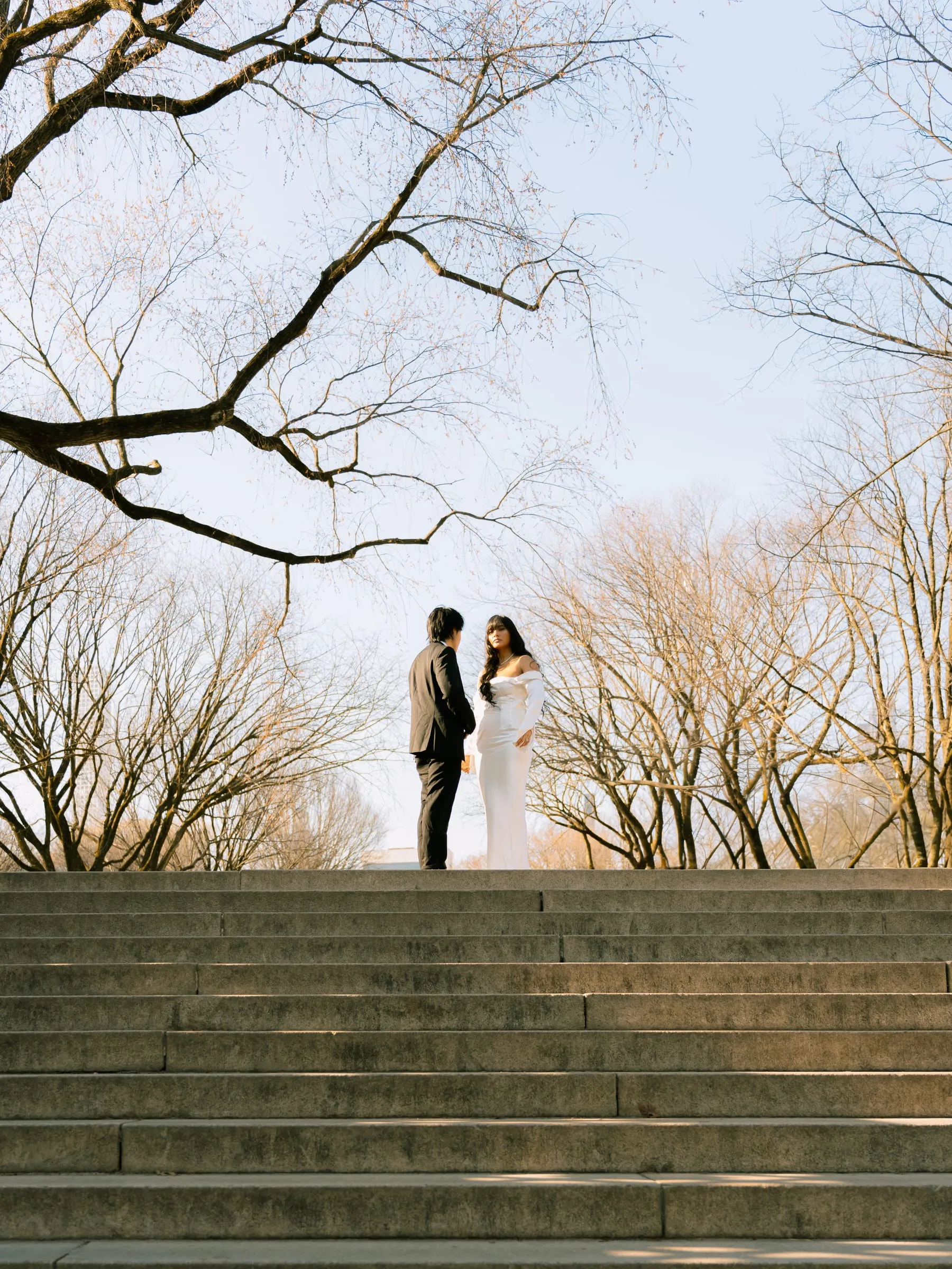 Noushin and Nathan standing together at the top of the park stairway among bare trees