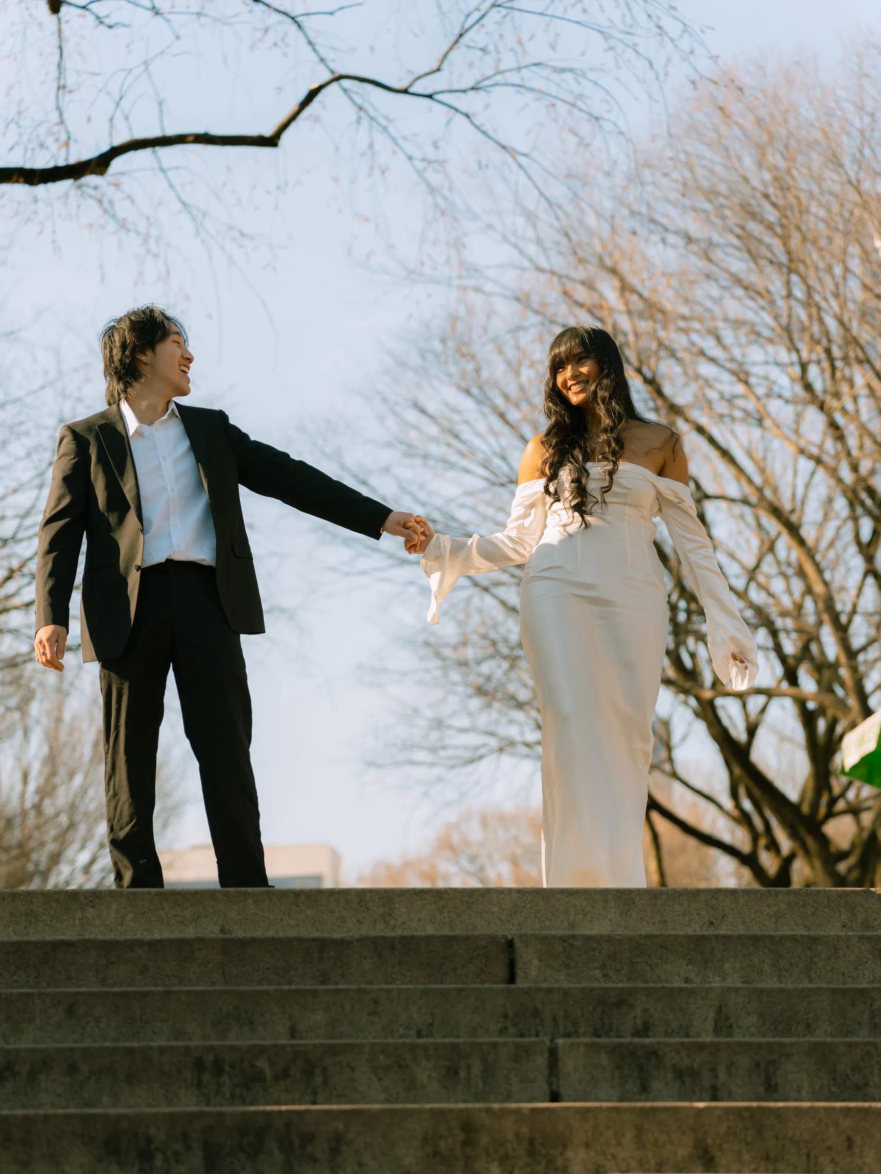 Noushin and Nathan smiling and holding hands atop the stone steps