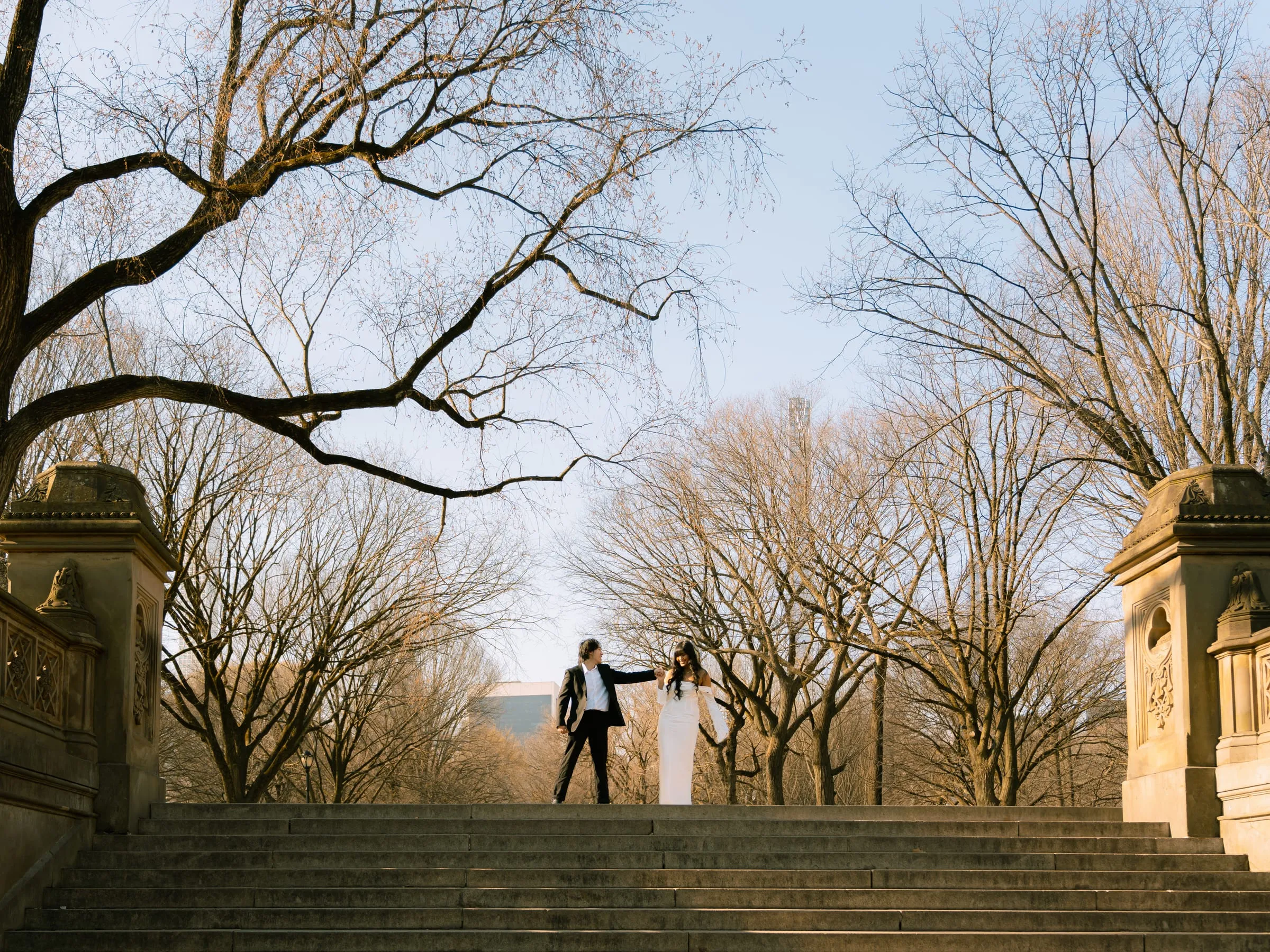Noushin and Nathan holding hands at the top of the stone stairway among the bare trees