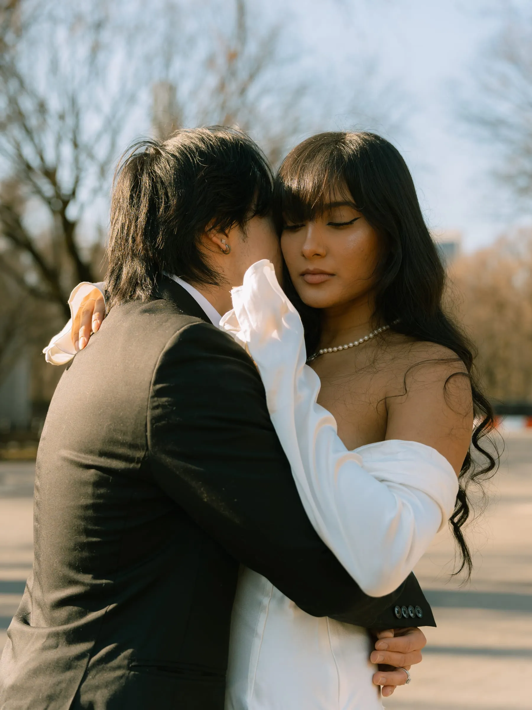 Noushin and Nathan in a close embrace, her eyes closed, the bare trees behind them