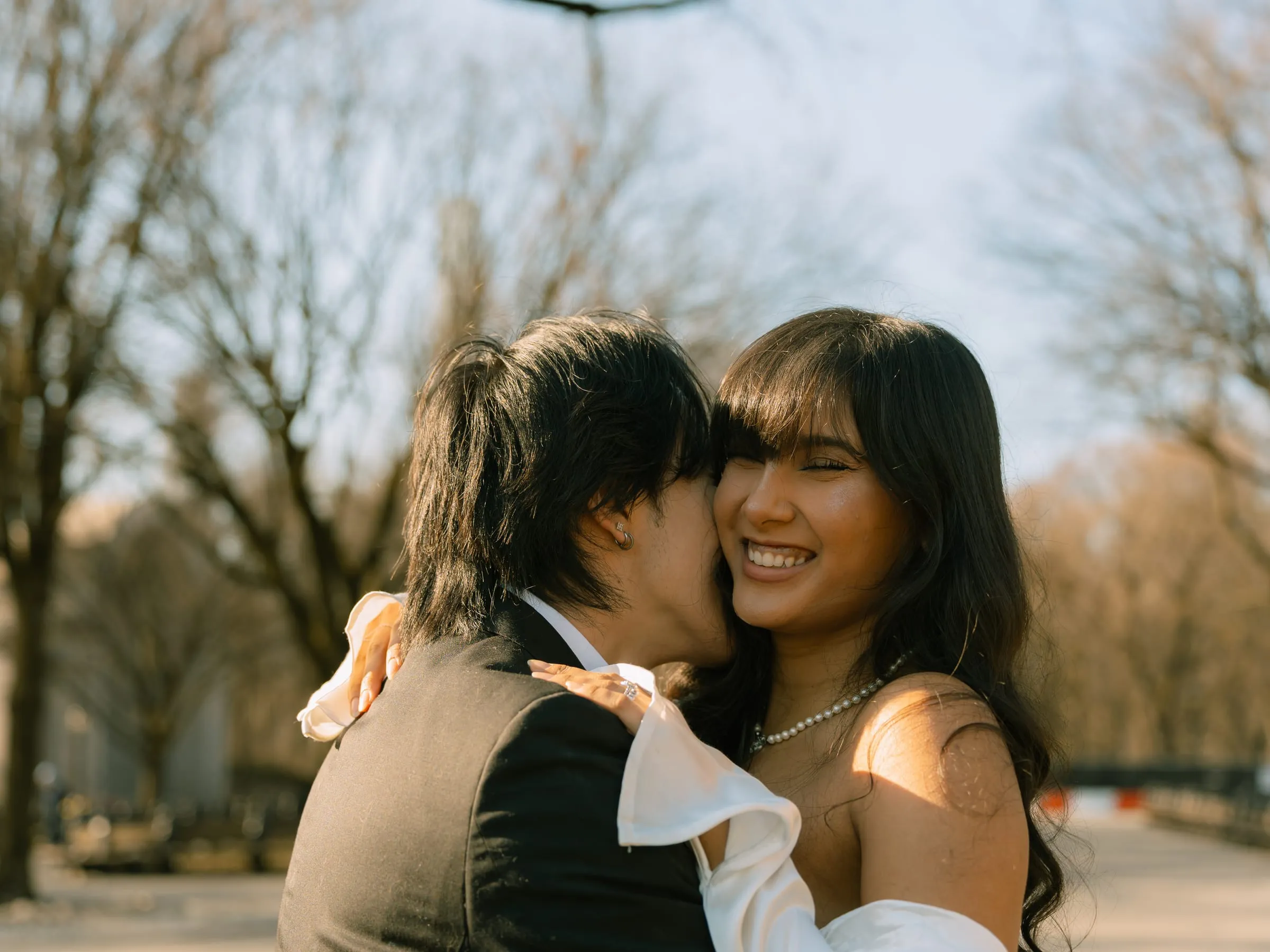 Noushin laughing as Nathan kisses her cheek on a sunny Central Park path