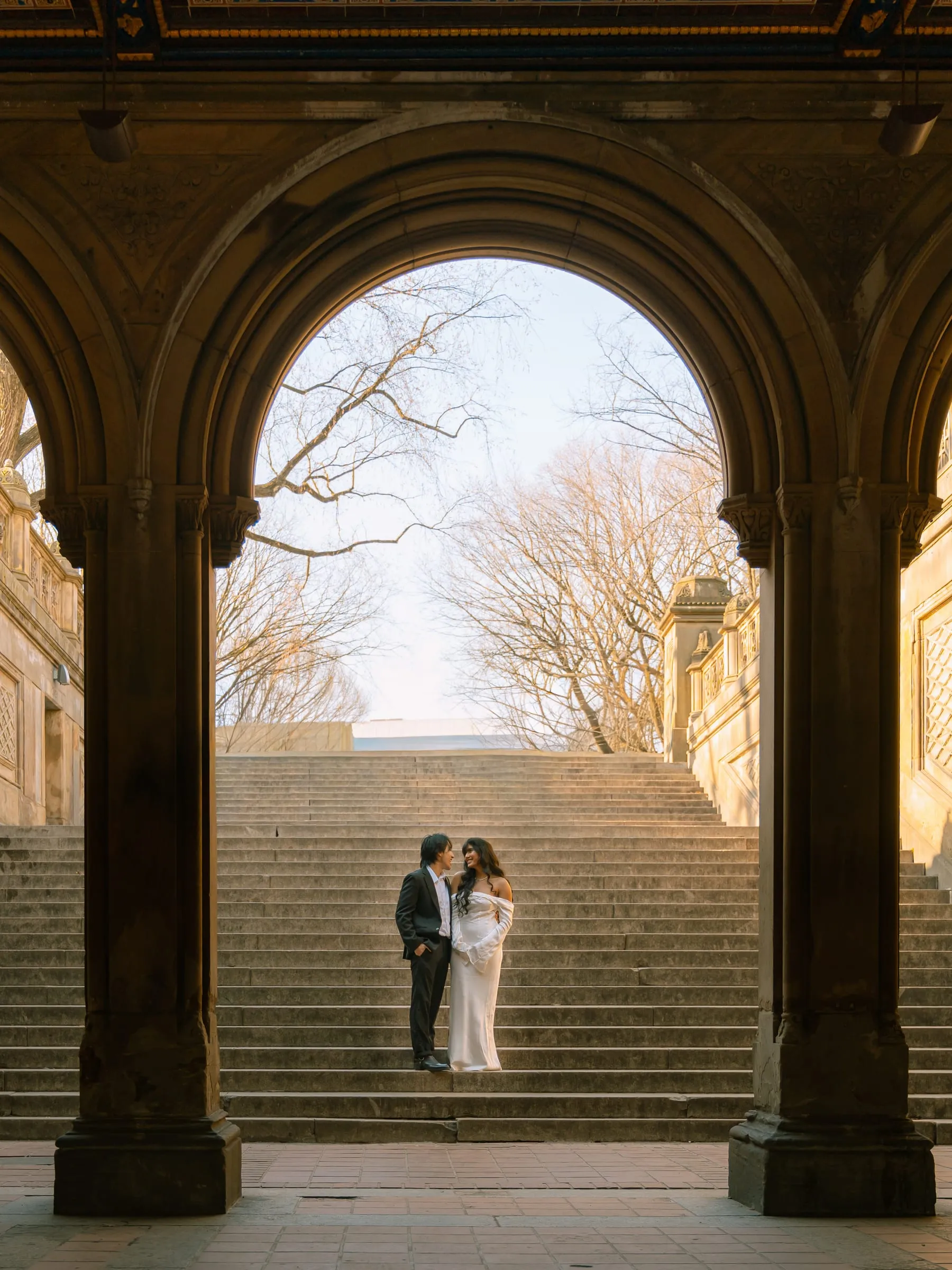 Noushin and Nathan standing together on the grand staircase, framed by one of Bethesda Terrace's arches