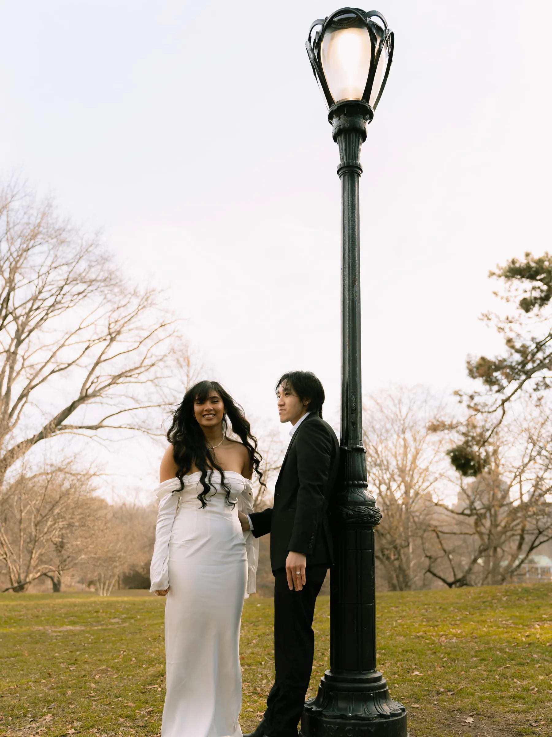 Noushin and Nathan standing together beside a park lamppost at dusk