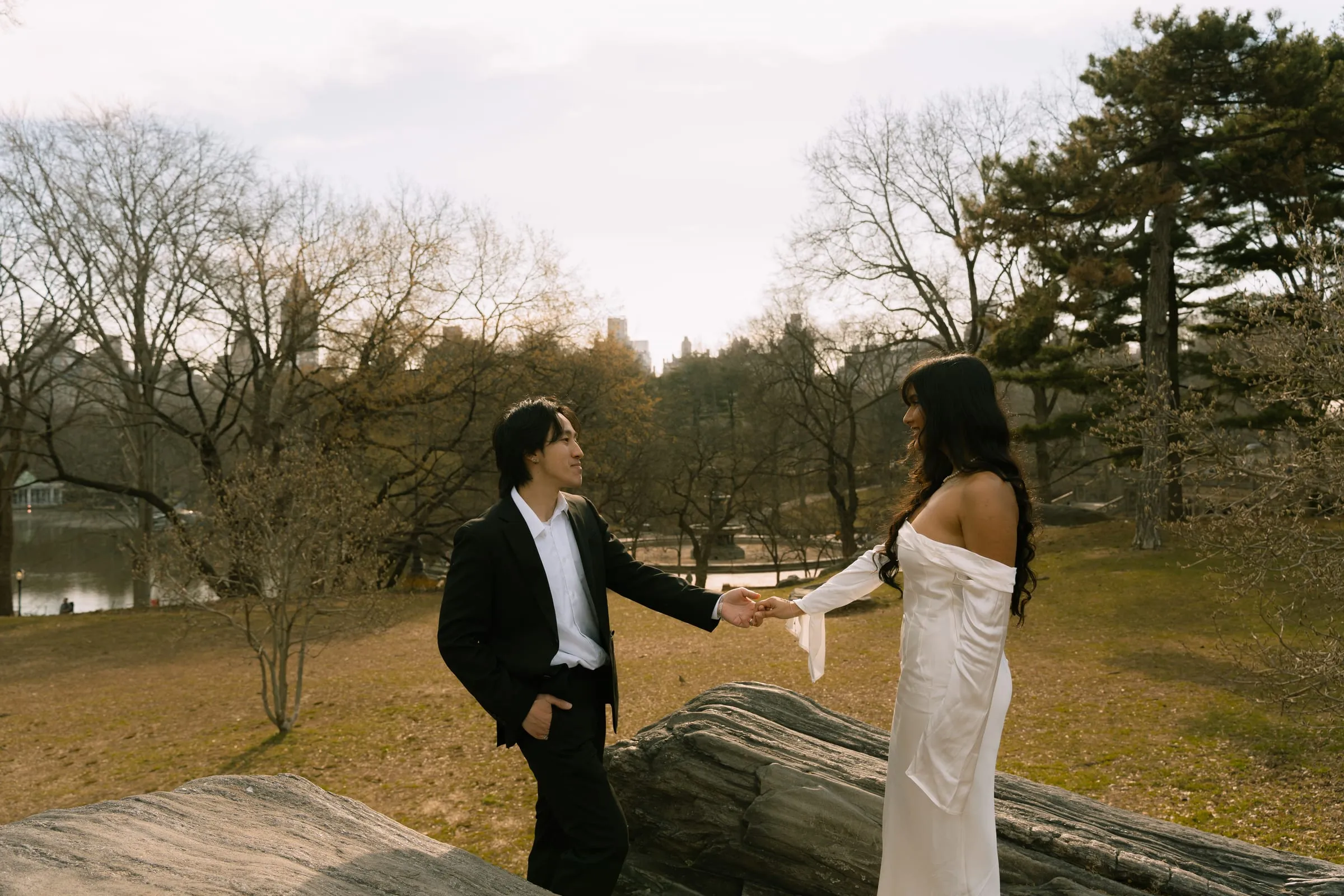 Noushin and Nathan holding hands atop a rock outcrop overlooking the lake, with the skyline behind them