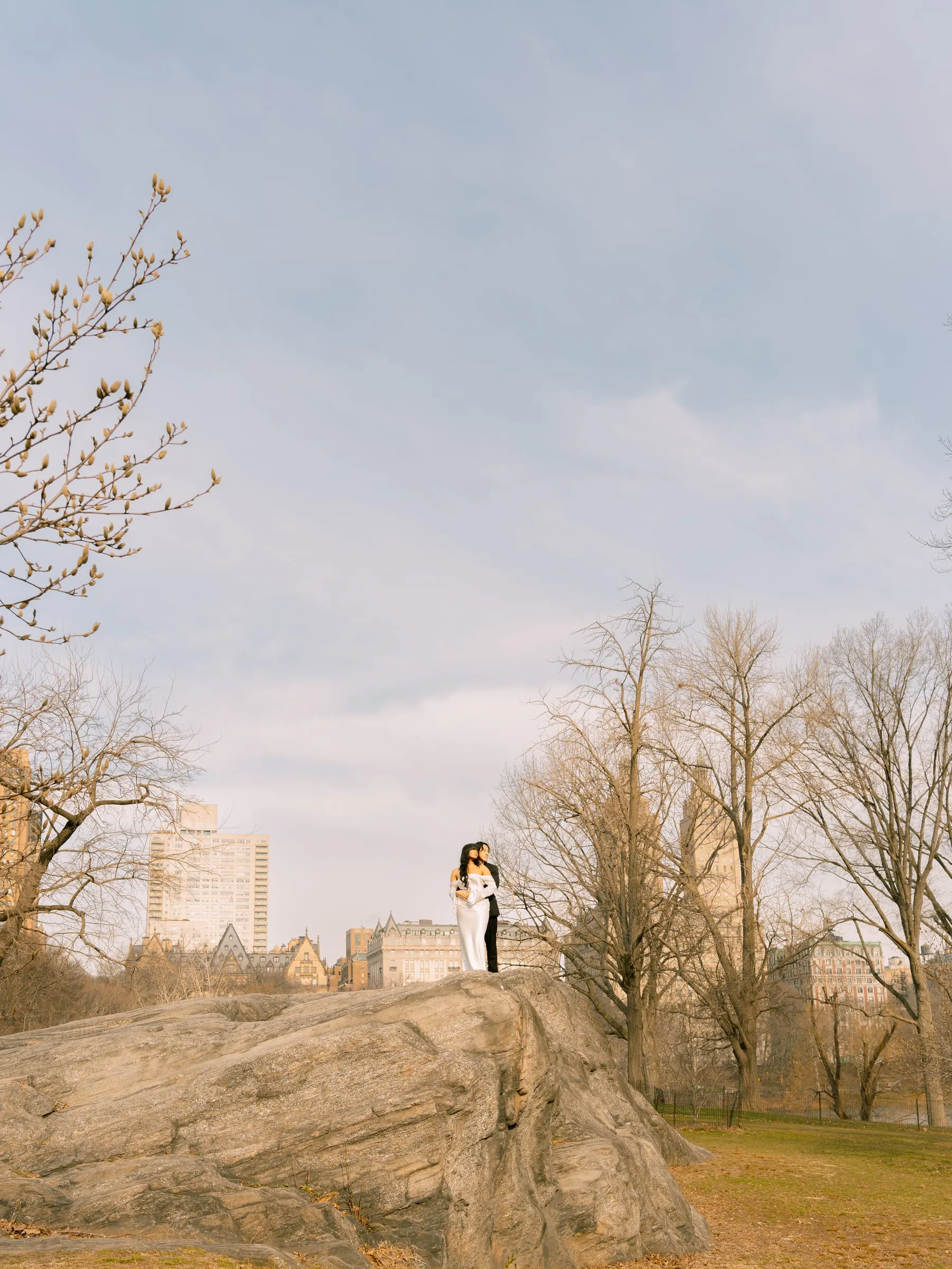 Noushin and Nathan standing together atop a rock formation with the Manhattan skyline in the distance