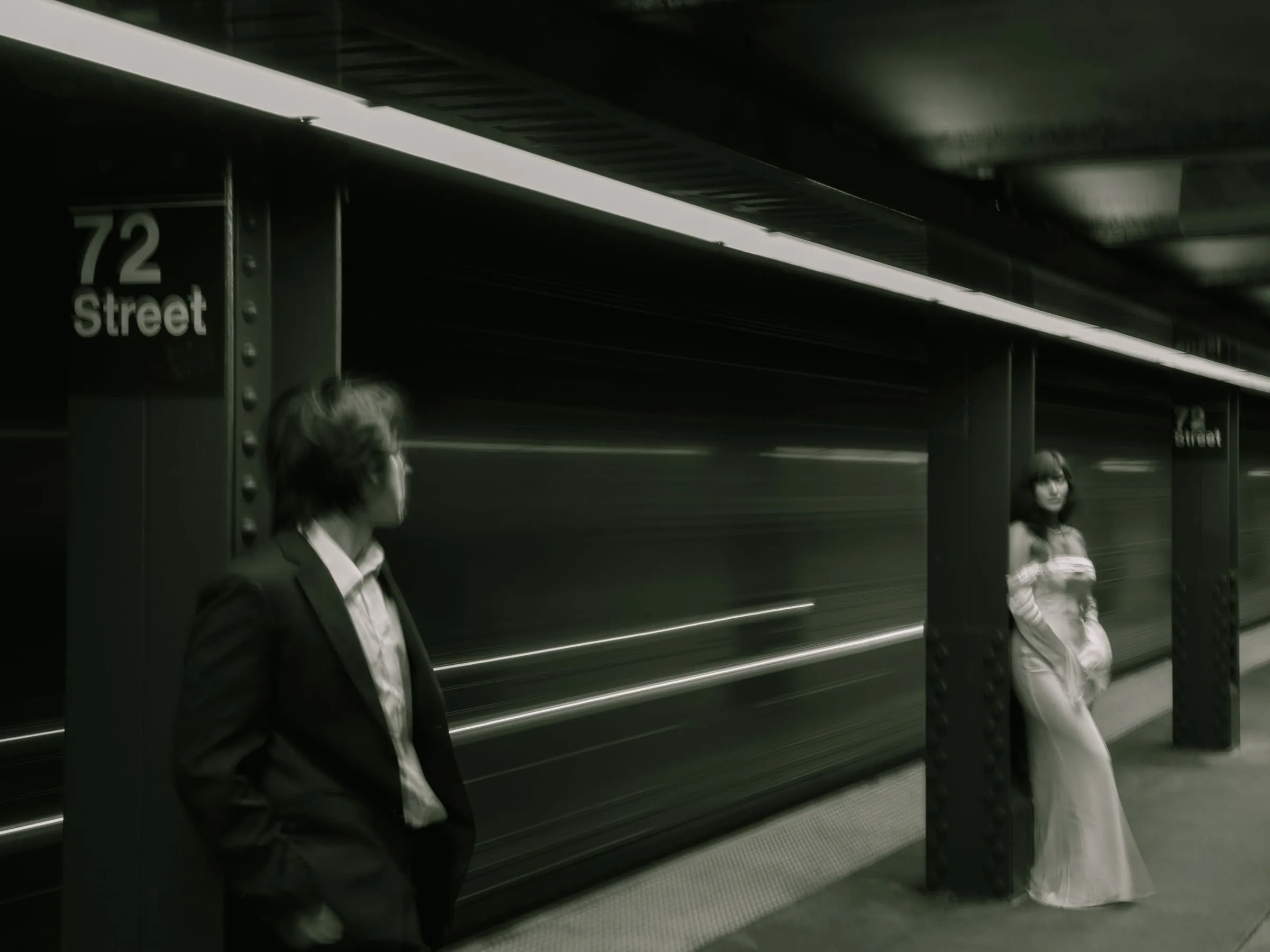 Noushin and Nathan standing on opposite sides of the 72nd Street subway platform as a train blurs past
