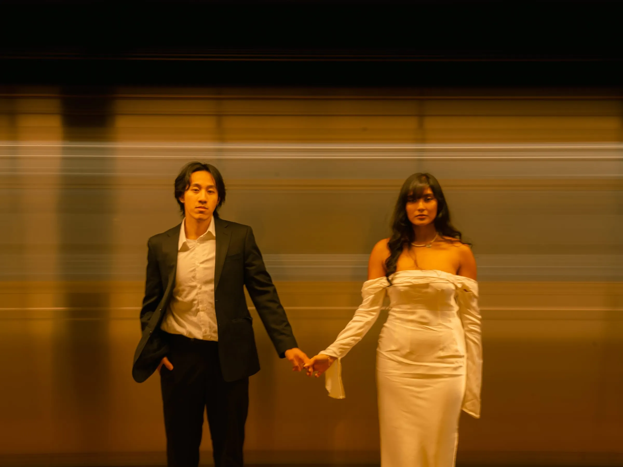 Noushin and Nathan holding hands in a station corridor, the warm light blurring around them