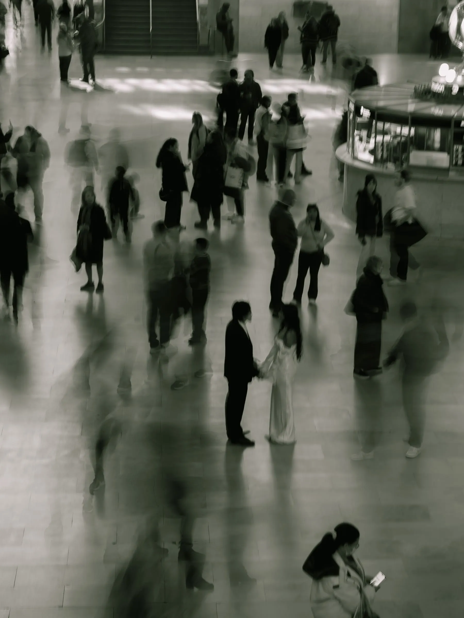 Noushin and Nathan holding hands in the Grand Central concourse as travelers blur past them
