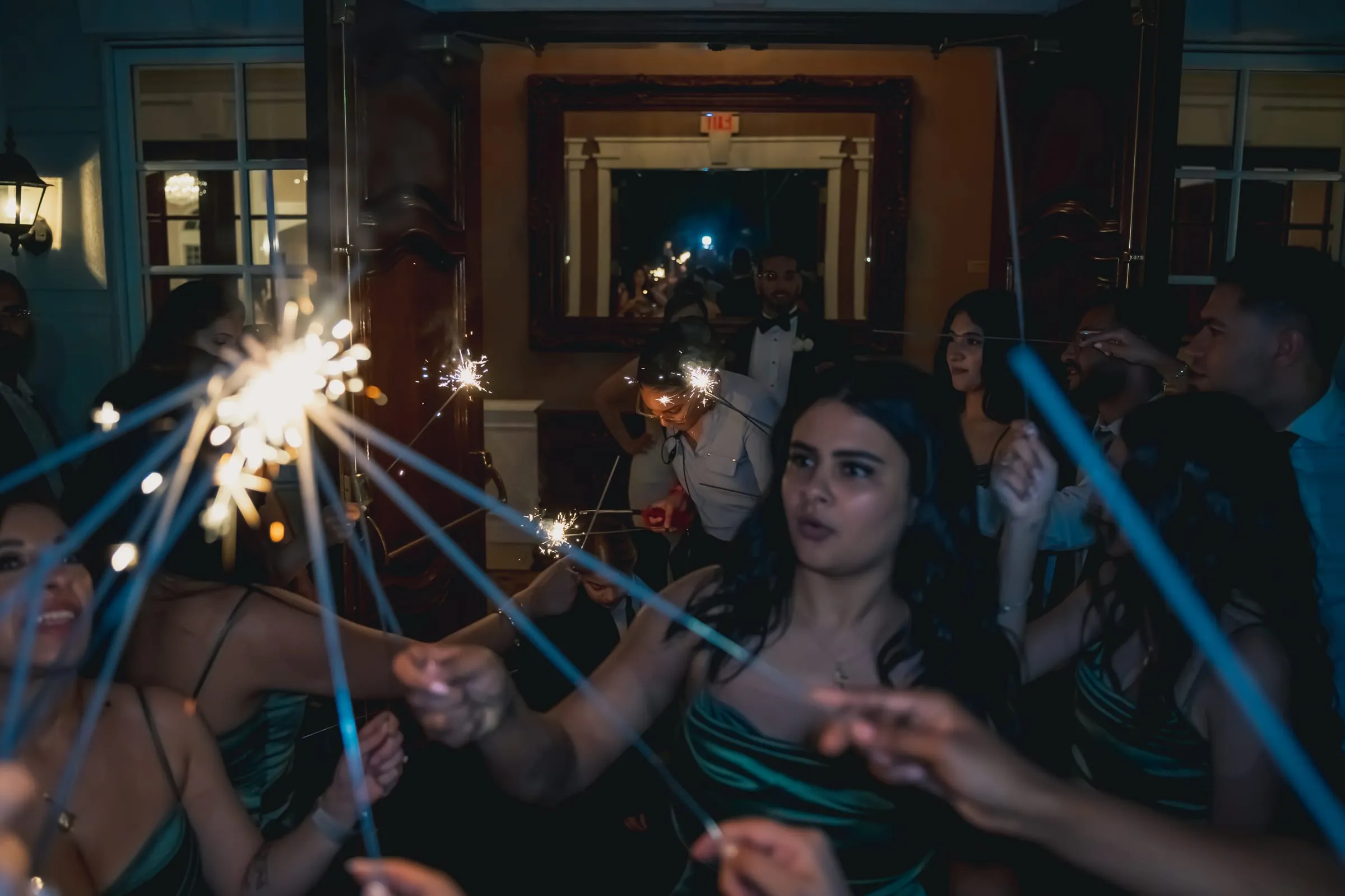 A bridesmaid in green satin lighting sparklers with guests inside Foxchase Manor