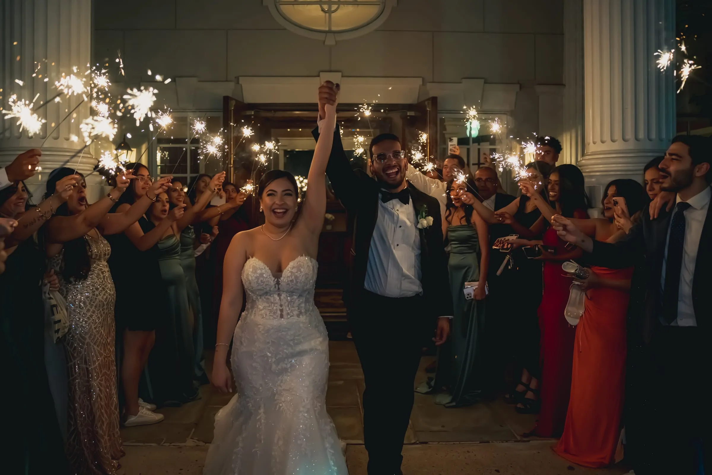 Sandy and Steph lifting their joined hands high as guests in green and red cheer