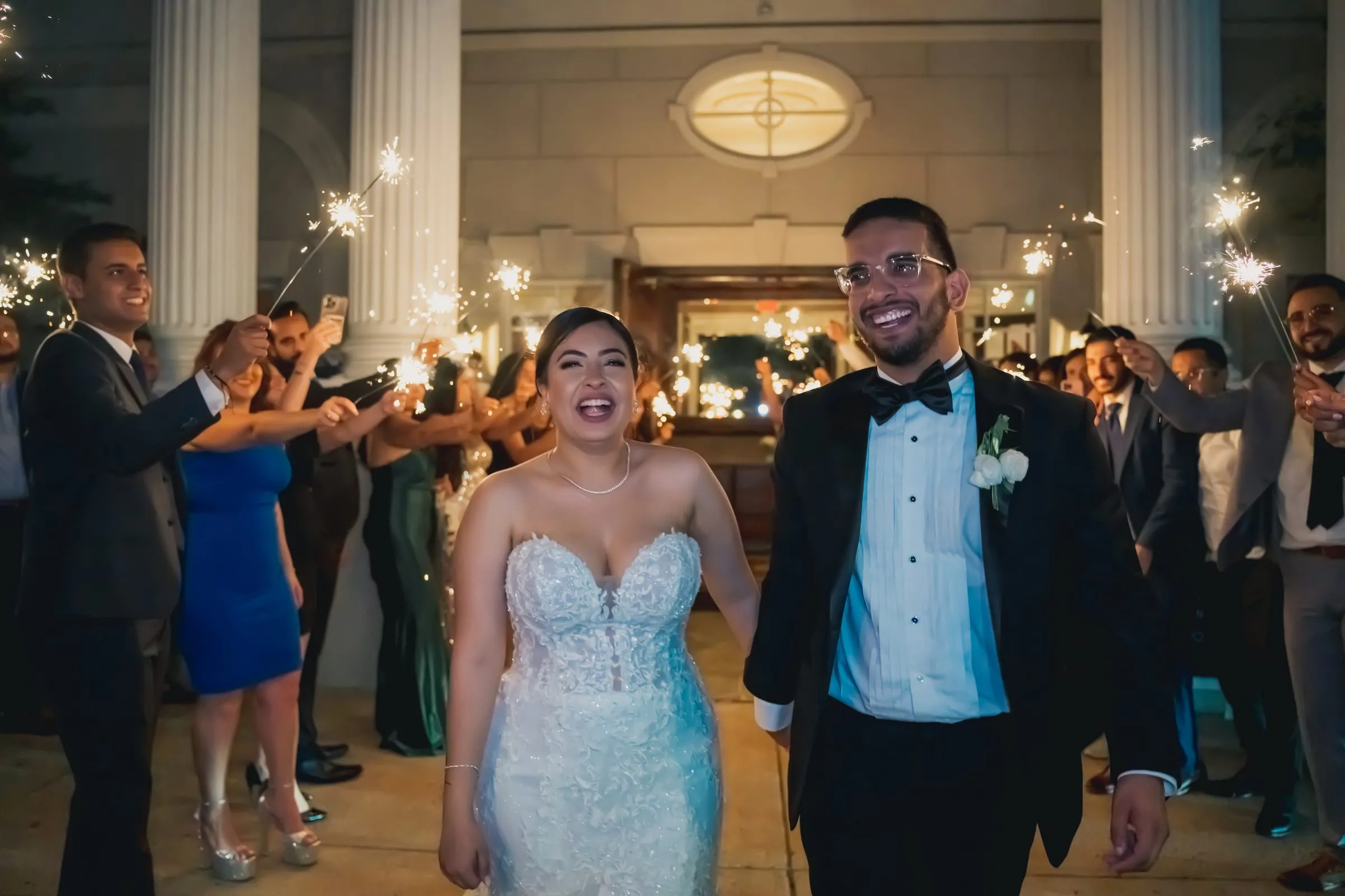 Sandy and Steph walking hand in hand toward the camera, guests clapping behind them