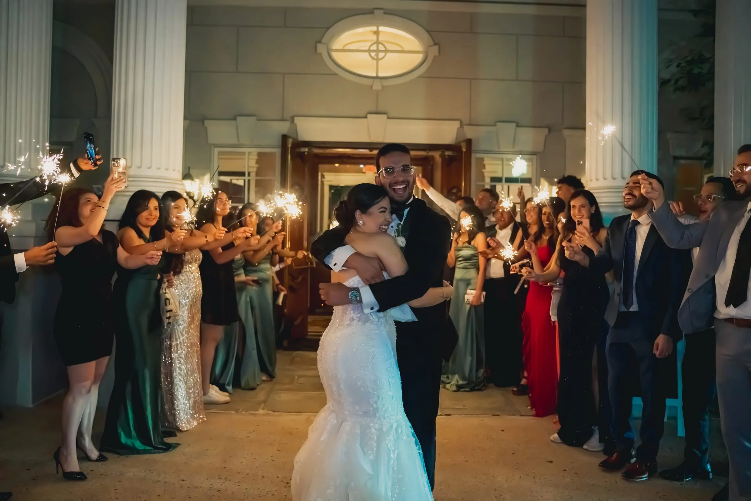 Sandy and Steph hugging and laughing as guests hold sparklers overhead