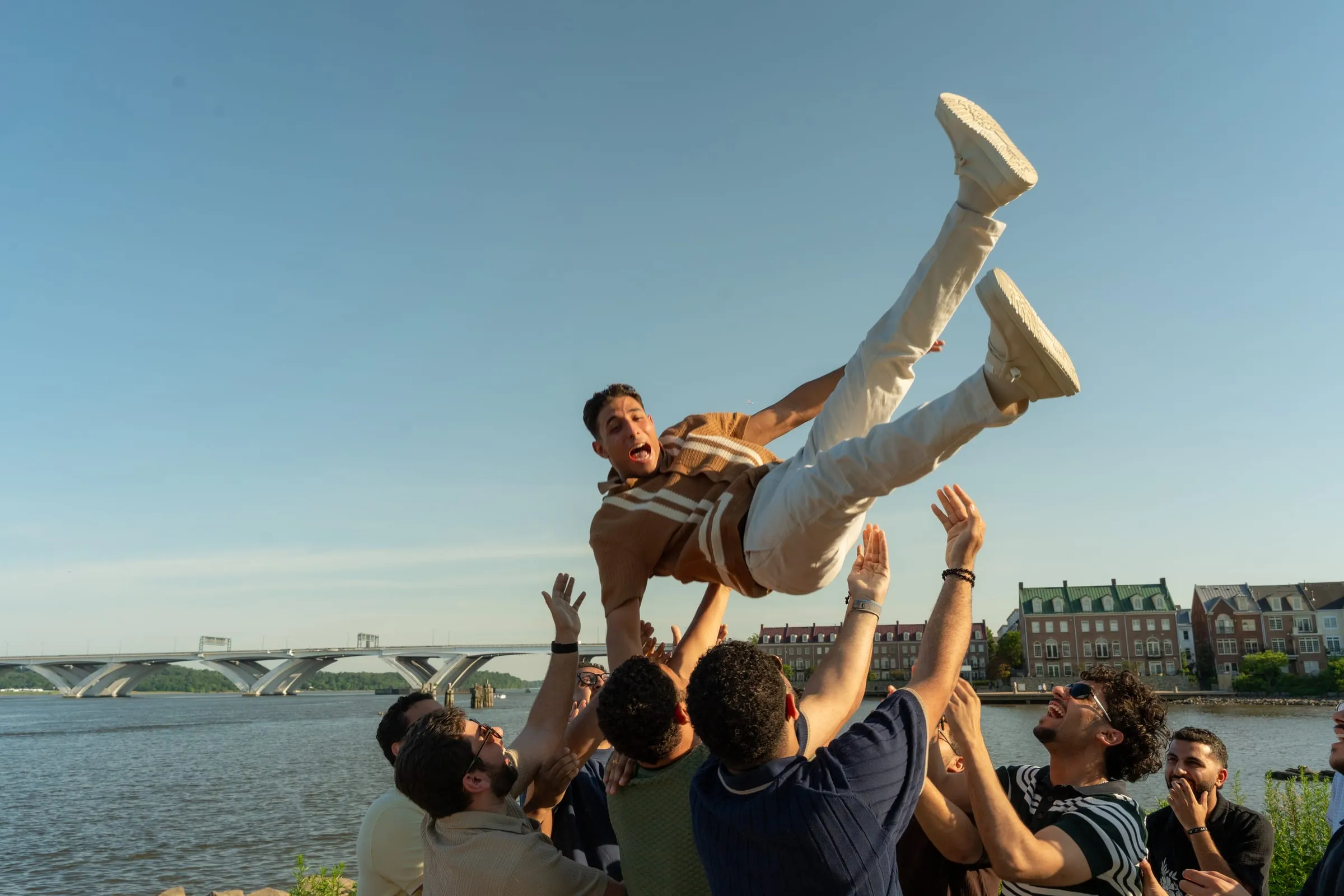 Thomas's friends celebrating by tossing him into the air beside the river